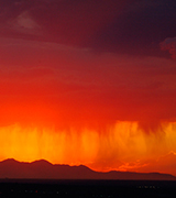 Photo of orange rain streaming from red clouds against a yellow sky over dark hills.
