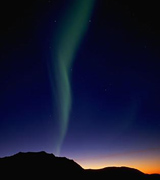 Aurora borealis against an indigo sky above dark hills.