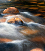 Stream water flowing over smooth stones.