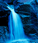 Blue waterfall on dark rocks.