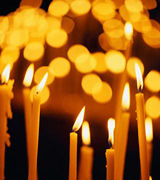 Slender lit candles, with those in back blurred like golden coins.