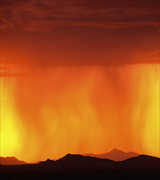 Photo of orange rain streaming from red clouds against a yellow sky over dark hills.