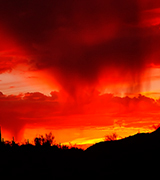 Rain streaming from red clouds over the desert at sunset.