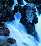 Icy blue mountain waterfall flowing over rocks.